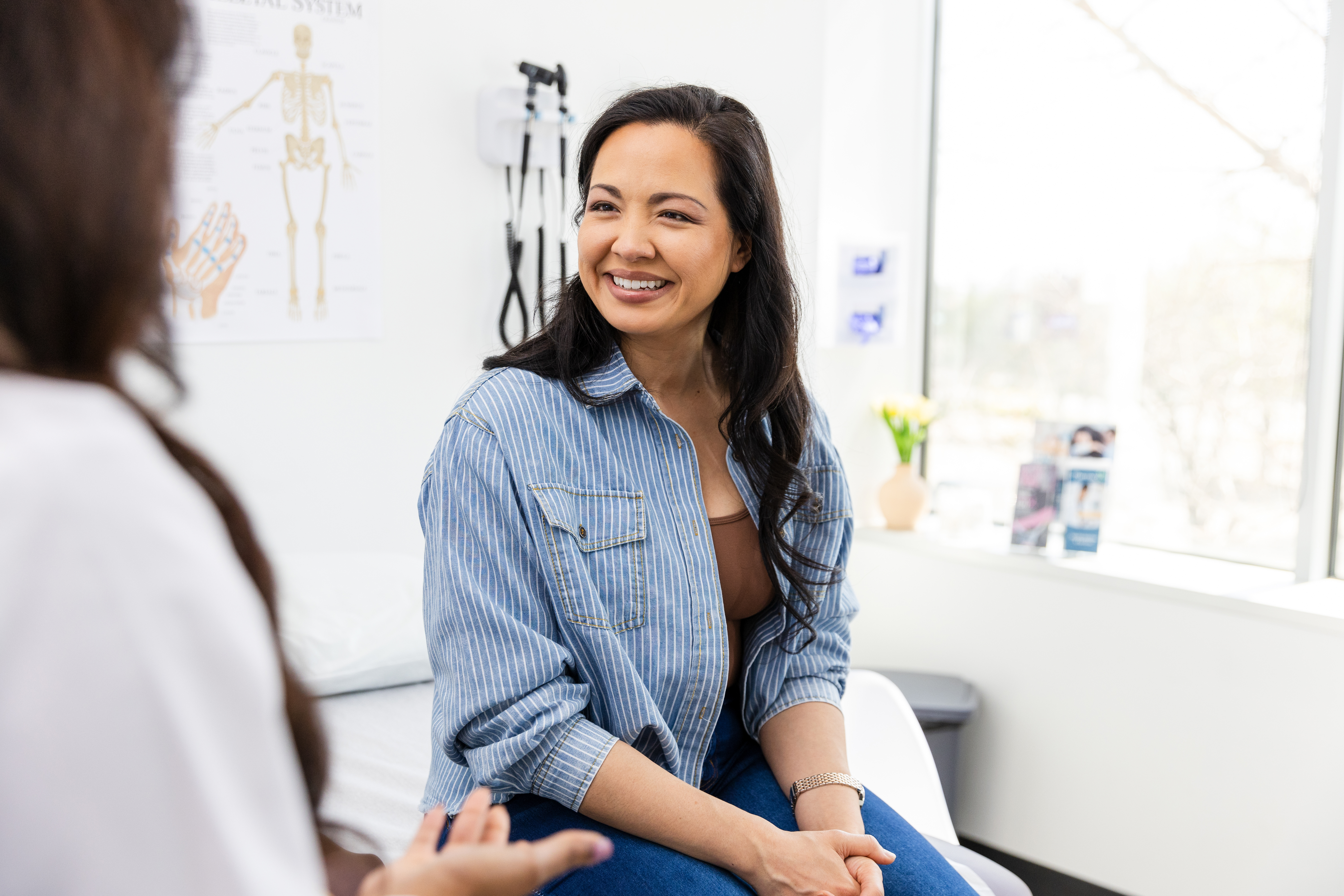 Mid adult female patient smiles while listening to the unrecognizable female doctor
